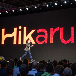 In the heart of a bustling tech conference, the vibrant 'Hikaru' logo jumps off a digital screen. Set against a stark black background, the fiery letters seem to flicker and dance, emanating a pulsating glow as if charged with the power of digital dreams.