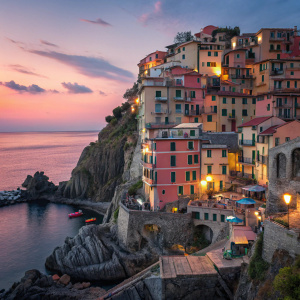 Twilight view of Manarola village, Cinque Terre, Italy. Colorful facades, warm lights, steep cliffside, stacked buildings with balconies.