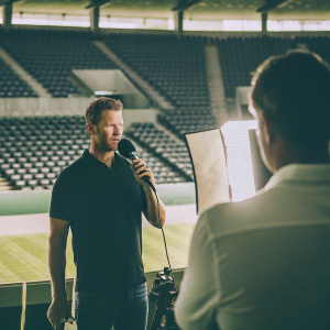 Julian Nagelsmann, wearing a black polo shirt, gives an interview. Empty football stadium backdrop