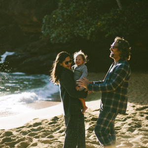 Matthew McConaughey with his family: Camila Alves, Vida Alves McConaughey, and Levi Alves McConaughey. Vida in plaid outfit. Backdrop of a sunny beach.