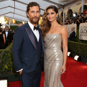 Matthew McConaughey, in a navy suit, and Camila Alves, in a silver gown, attending the Golden Globe Awards. Crowd and red carpet visible