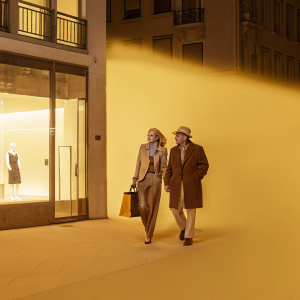 Patrick Stewart and Wendy Neuss walking through a bustling city street at night. Brightly lit shop windows and neon signs illuminate their path. A silhouette of a woman watching from a nearby balcony.