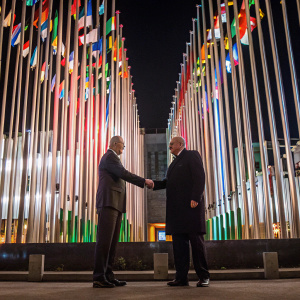 Formal handshake between Gianni Infantino and Florentino Pérez at FIFA gala. Multicolored backdrop featuring world flags.