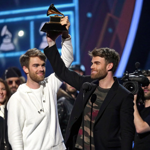 Andrew Taggart and Alex Pall of The Chainsmokers at the Grammy Awards. Accepting trophy, surrounded by flashing cameras and celebrities.