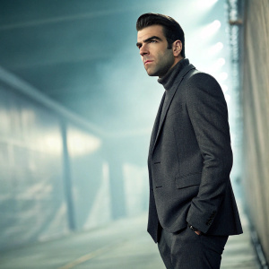 Zachary Quinto, intense gaze, wearing a charcoal suit. Promotional photo shoot, abstract blurred background.
