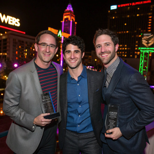 Stephen Friedman, Darren Criss, and Chris McCarthy celebrating at the NewNowNext Awards 2014. Neon-lit cityscape backdrop.