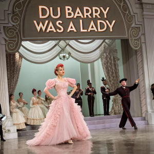 Movie poster for 'Du Barry Was A Lady'. Lucille Ball in a stunning pink gown, Red Skelton and Gene Kelly surrounded by dancers in elaborate costumes. Ornate drapery and a grand stage setting. Traditional movie lobby card style.