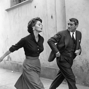 Sophia Loren and Cary Grant mid-motion on set of 'The Pride and the Passion'. 1957. Black and white photo. Dark blouse and skirt on Loren. Formal suit on Grant. Against plain, textured wall.
