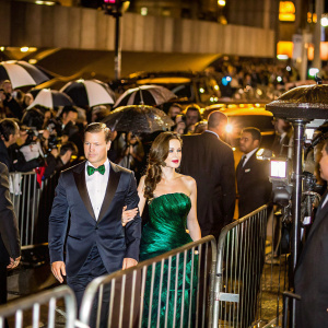 Brad Pitt and Angelina Jolie arriving at the Met Gala. Angelina in a stunning green velvet gown, Brad in a navy tuxedo. Crowded backdrop of paparazzi and celebrities.