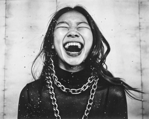 A close-up portrait of laughing hard, Korean 
 Karina Aespa with sharp features, wearing a black turtleneck and heavy silver chain jewelry. He has large silver chain earrings. Two horizontal beams of red light illuminate his face, creating a dramatic and futuristic effect. His expression is intense and captivating, with his eyes wide and lips slightly parted. The background is a stark white, emphasizing the contrast between light and shadow.