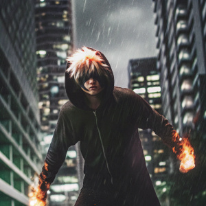 Katsuki Bakugo, from My Hero Academia, standing in a fierce pose. Wearing a black hoodie with flames. Dark urban cityscape background