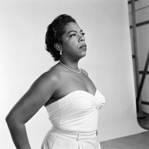 Della Reese, African American singer and actress. Wearing a white halter top, she stands in a plain, light-colored studio. Black and white photo, serious expression