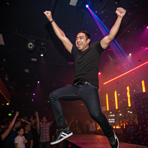 Marco Fabian, midair celebration. Dressed in black t-shirt and dark jeans. Flashy nightclub background, surrounded by cheering fans
