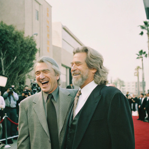 Robert De Niro and Jeff Bridges laughing together at the Hollywood Film Awards. Red carpet event, surrounded by flashing cameras.