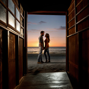 Megan Fox and Brian Austin Green on a deserted beach. Sunset behind them. Both are in casual wear.