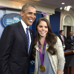 Former US President Barack Obama with Olympic gymnast McKayla Maroney. Both smiling at the camera. White House press room setting.