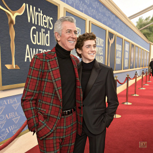 Frank Gilroy and Tony Gilroy, father and son duo, posing on the carpet at the Writers Guild Awards. Frank in a plaid jacket and black turtleneck, Tony in a dark tailored suit.