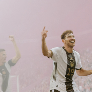 Leon Goretzka, smiling, during a Bundesliga match. Wearing jersey with number 19, celebrating a goal. Crowded stadium in the background, with a referee nearby.