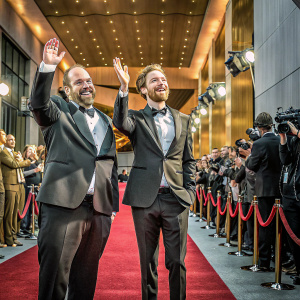 Paul Giamatti and Robert Pattinson at the Oscars, dressed in tuxedos, beaming and clapping. Red carpet event