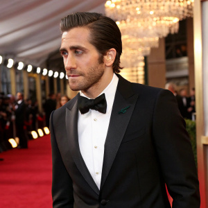 Jake Gyllenhaal at a glitzy award show. Black tuxedo, slicked-back hair, clean-shaven look