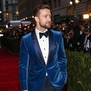 Justin Timberlake, at the Met Gala, dressed in a deep blue velvet tuxedo with silver details. Standing on a busy street with flashing cameras and paparazzi.