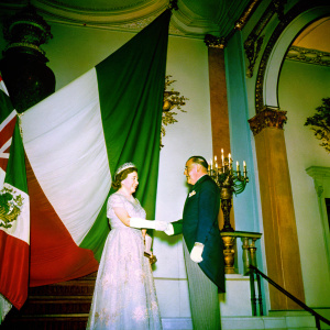 Queen Elizabeth II and Eduardo Medina-Mora, the Mexican Ambassador, at a diplomatic ceremony. Handshake in front of large flag