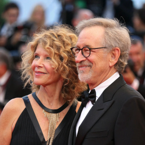 Steven Spielberg and Kate Capshaw at the Venice Film Festival. Spielberg, bearded, glasses, Capshaw, curly hair, smiling. Crowded backdrop