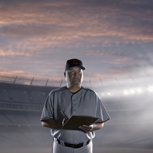 Terry Francona, intense gaze, stands in front of a blurred stadium. Holding a clipboard, dressed in a Cleveland Indians jersey and cap.
