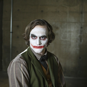 Close-up of Joaquin Phoenix as The Joker. Intense, white-painted face, dark makeup, and a menacing expression. Black background.