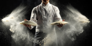 White flour flies in air on black background, pastry chef claps hands and prepares yeast dough for pizza pasta