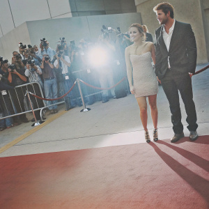 Miley Cyrus and Liam Hemsworth attending the premiere. Red carpet event, paparazzi flashing.