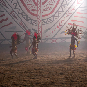 Paul Simon's 'The Rhythm of the Saints' album art. Incan dancers in vibrant attire, blending traditional moves with modern energy. Set against a dim, earth-toned background with fiery red highlights from their headdresses.