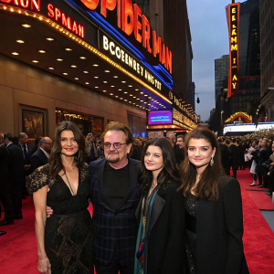 Ali Hewson, Bono, Eve Hewson, and Jordan Hewson at a Spider-Man Broadway show premiere. Crowded theater lobby. Neon signs and red carpet.