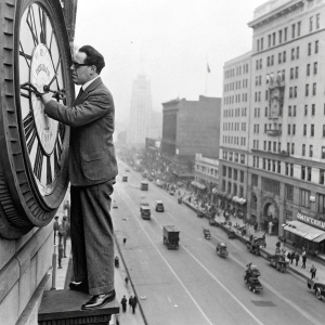 Silent film actor Harold Lloyd, standing on a clock tower in a classic pose, amidst a bustling early 20th century city street.