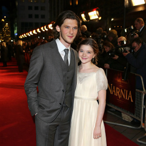 Ben Barnes in a grey suit, Georgie Henley in a white dress, attending the world premiere of 'Narnia' at Odeon Leicester Square. Crowded red carpet scene.