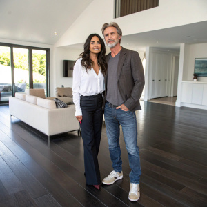 Emmanuelle Chriqui and Sam Trammell, actors, standing in a modern minimalist living room. The floor is made of dark wooden planks.