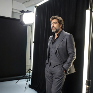 Javier Bardem, starring in an interview, donning a grey suit. Bright studio lighting, sleek black backdrop.