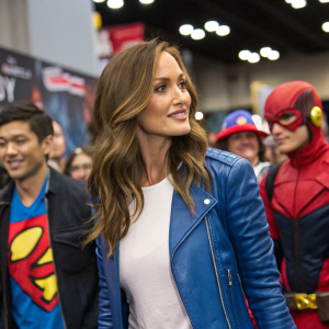 Minka Kelly, at New York Comic Con, wearing a blue leather jacket over a white shirt. Standing amidst fans and cosplayers.