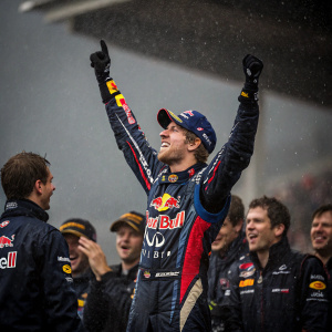 Sebastian Vettel in victory celebration. Surrounded by team in Red Bull uniforms. Dark, wet backdrop