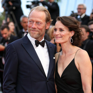 Iain Glen and Charlotte Emmerson at Cannes Film Festival premiere. Both are dressed formally, with Iain in a tailored suit and Charlotte in a black evening gown.