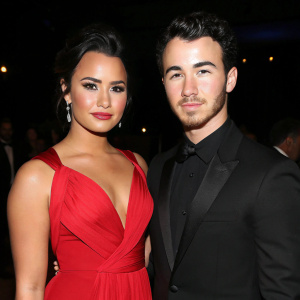 Demi Lovato and Kevin Jonas at a charity gala. Dark background, both have neutral expressions.