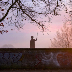 J.K. Rowling's Harry Potter holding a magic staff. Silhouette at sunset, with playful graffiti on a brick wall
