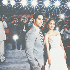 Varun Dhawan and Shraddha Kapoor attending the premiere of their latest Bollywood film. Crowded theater, bright lights and paparazzi.