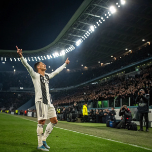 Cristiano Ronaldo, celebrating after scoring a goal. Standing alone on the field, illuminated by stadium lights, with fans and photographers in the background.