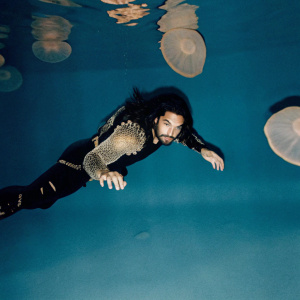 Jason Momoa, playing Aquaman, in a underwater scene surrounded by giant jellyfish.