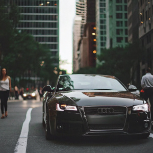 A sleek, black Audi RS5 convertible parked on a bustling city street, surrounded by tall office buildings.
