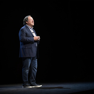 Robert M. Bakish, CEO of Viacom, addressing the audience. Black background, dimly lit stage with spotlight on him.