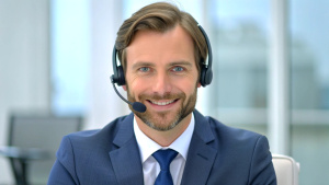 Handsome male call center operator in headset working in modern office. Hotline support service concept