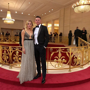 Sienna Miller and Channing Tatum at a stylish fashion gala. They stand on a luxurious red carpeted stage with intricate golden fence.