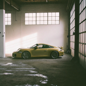 A sleek yellow Porsche 911 GT3 RS parked in a garage. Neon lights casting shadows
